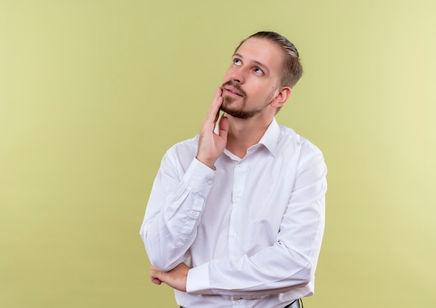 Handsome businessman in white shirt looking aside with pensive expression standing over olive background