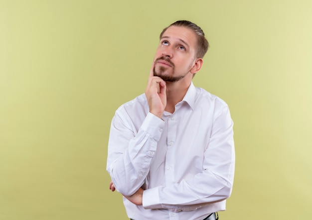 Handsome businessman in white shirt looking up puzzled standing over olive background