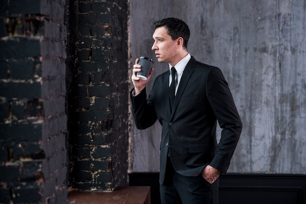 Handsome businessman with coffee cup and hand in pocket