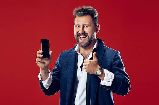 Красивый бизнесмен с мобильным телефоном. Счастливый деловой человек, стоящий на красном фоне студии. Красивый мужской поясной портрет