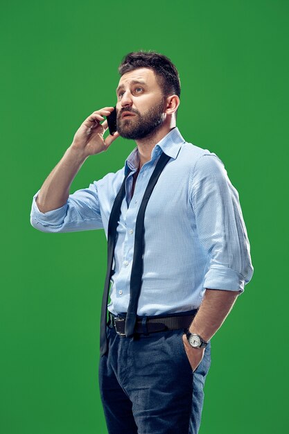 Красивый бизнесмен с мобильным телефоном. Серьезный деловой человек, стоящий на фоне зеленой студии