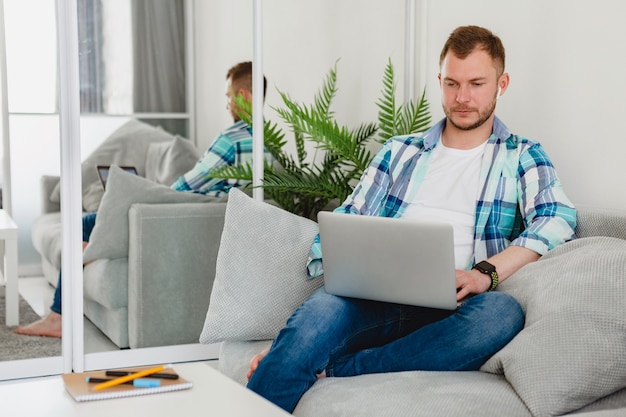 Красивый занятый сосредоточенный мужчина в рубашке расслабленно сидит на диване у себя дома за столом, работая онлайн на ноутбуке из дома