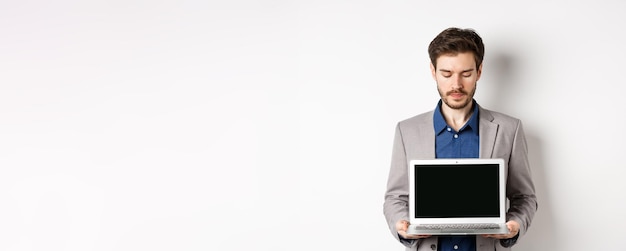 Free photo handsome caucasian businessman in suit showing empty laptop screen demonstrate promo standing on whi