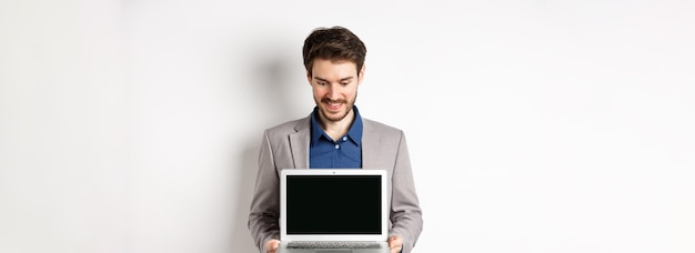 Free photo handsome caucasian businessman in suit showing empty laptop screen demonstrate promo standing on whi