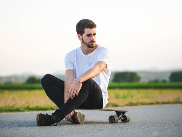 Handsome Caucasian male sitting on a skateboard at outdoors