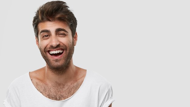 Handsome Caucasian man has fun and laughs over funny joke, shows white teeth, being in high spirit