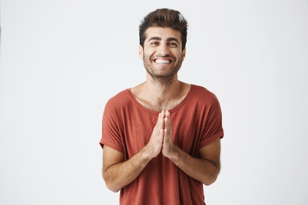 Handsome caucasian man in red T-shirt smiling happily and clapping hands surprised with birthday gift from friends. Closeup portrait of unshaven guy sharing positive vibes.