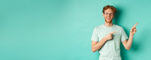 Free photo handsome caucasian man with ginger hair wearing glasses and tshirt pointing fingers right and smilin