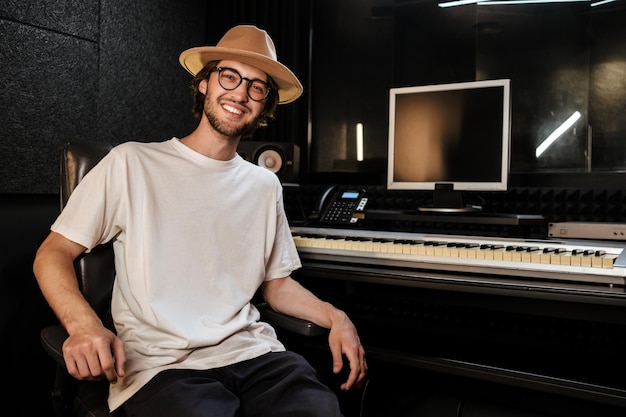 Bel ragazzo allegro che guarda felicemente a porte chiuse nel moderno studio di registrazione del suono. giovane musicista alla moda che lavora in studio