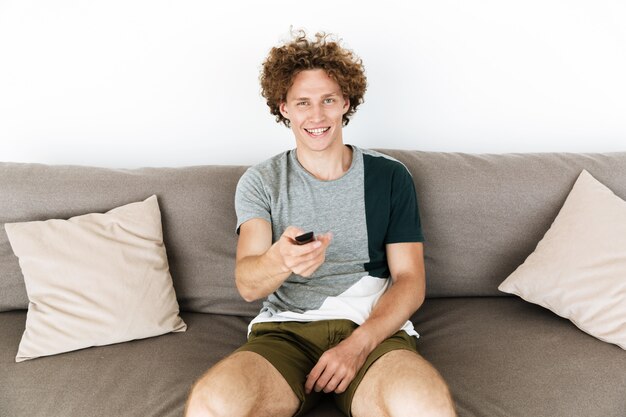 Handsome cheerful man sitting on sofa holding remote control