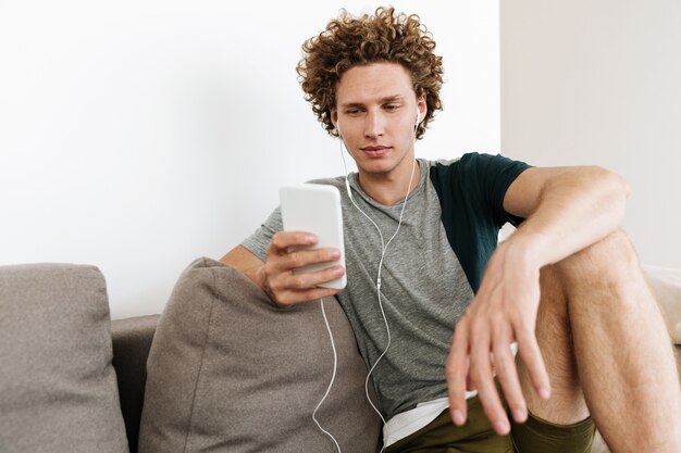 Handsome concentrated man sitting at sofa using mobile phone