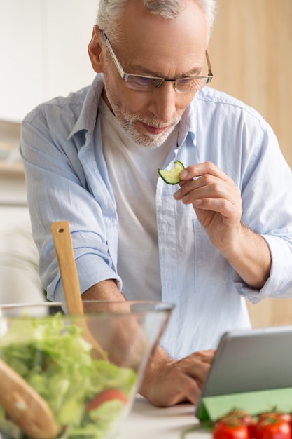 Handsome concentrated mature man cooking salad using tablet