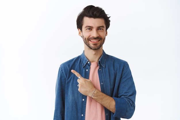 Handsome confident bearded man in stylish outfit pointing upper left corner smiling joyfully give advice where find best sale offers recommend product grin pleased standing white background