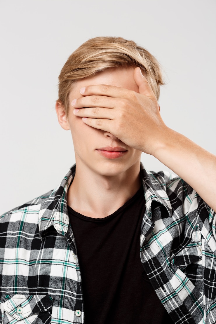 Free Photo handsome confident blond young man wearing casual plaid shirt covering eyes with hand, on grey wall