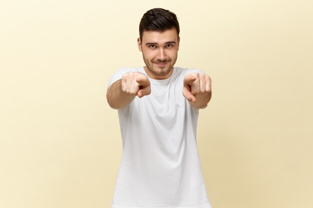 Free photo handsome confident positive young guy in white casual t-shirt pointing to the front