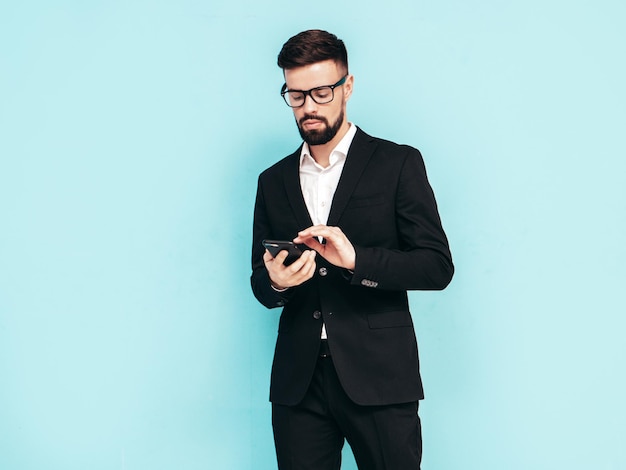 잘 생긴 자신감 있는 세련된 힙스터 램버섹슈얼 모델 우아한 검은 양복을 입은 섹시한 현대 남성 스튜디오에서 포즈를 취하는 패션 남성 스마트폰 들고 휴대폰 화면 보기 앱 사용