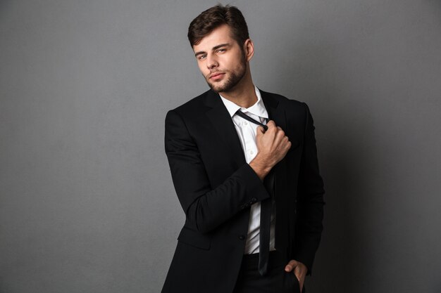 Handsome confident young business man in black suit straightening his tie