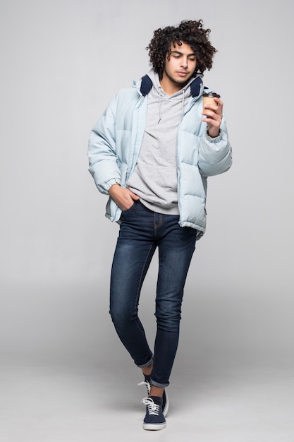 Handsome confident young curly haired man drinking coffee standing infront of isolated white wall