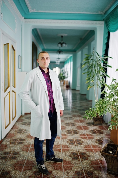 Free photo handsome and confident young doctor in white coat with stethoscope posing in the hospital