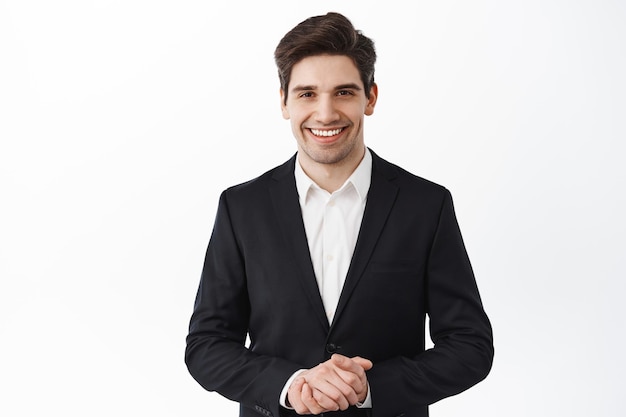 Free photo handsome corporate man, real estate agent assistant smiling, hold hands together, how may i help you, smiling friendly and polite, assist customer, white background