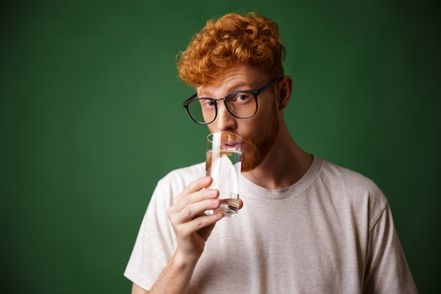 Handsome curly readhead bearded man in glasses, drinking water