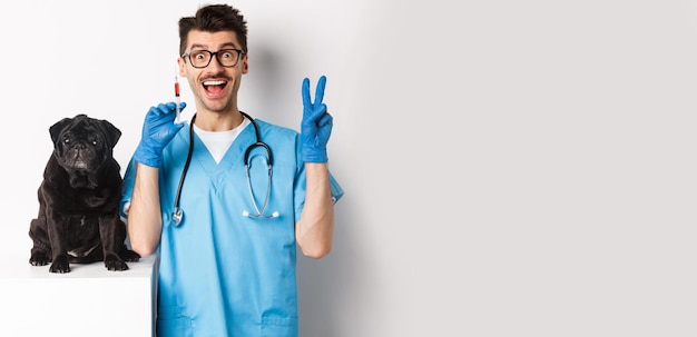 Free photo handsome doctor veterinarian holding syringe and standing near cute black pug vaccinating dog white