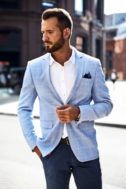 handsome fashion businessman model dressed in elegant blue suit posing on street