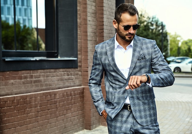 handsome fashion businessman model dressed in elegant checkered suit posing on street