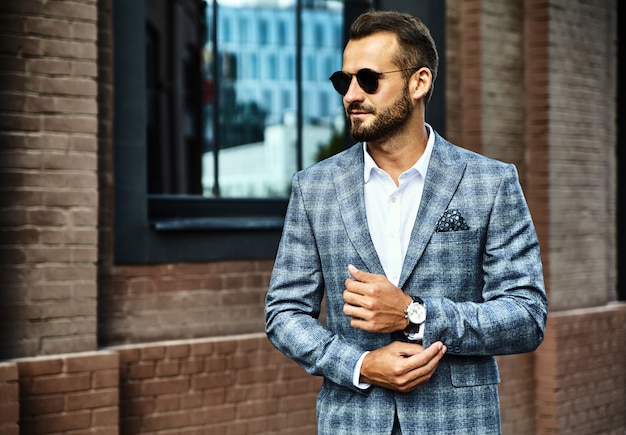 handsome fashion businessman model dressed in elegant checkered suit posing on street