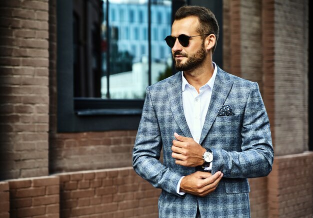 handsome fashion businessman model dressed in elegant checkered suit posing on street