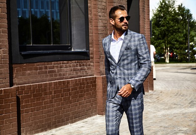 handsome fashion businessman model dressed in elegant checkered suit posing on street