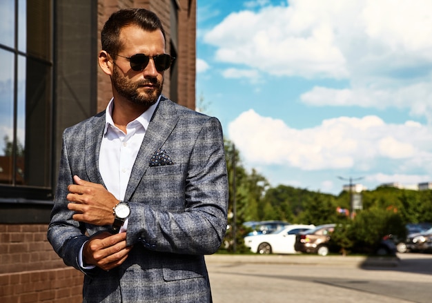 handsome fashion businessman model dressed in elegant checkered suit posing on street