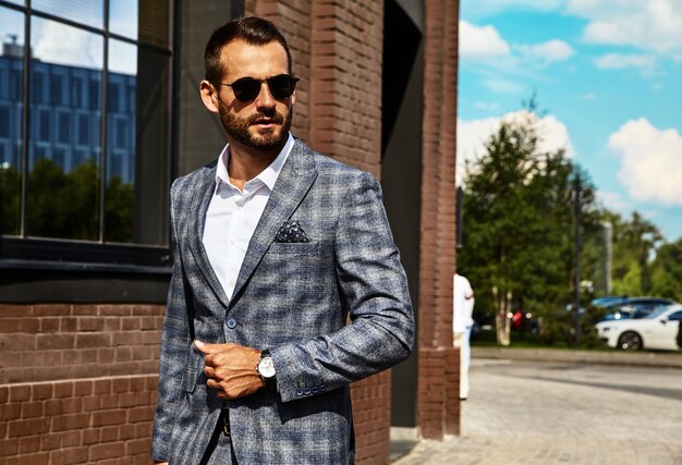 handsome fashion businessman model dressed in elegant checkered suit posing on street