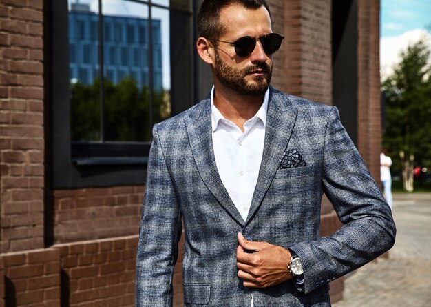 handsome fashion businessman model dressed in elegant checkered suit posing on street