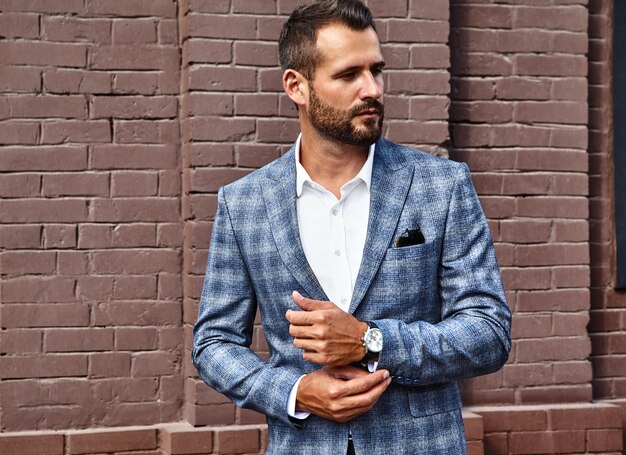 handsome fashion businessman model dressed in elegant checkered suit posing on street