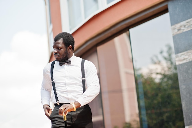 Free photo handsome fashionable african american man in formal wear bow tie and suspenders walking stick