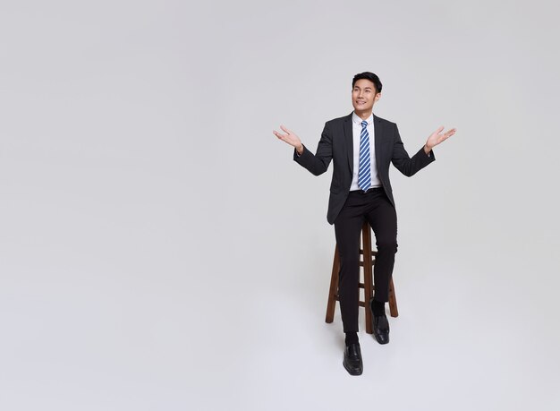 Улыбка азиатского бизнесмена красивого и дружелюбного лица в официальном костюме указывает его руки, чтобы скопировать пространство на белом фоне.