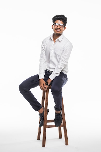 Handsome good looking Indian man sitting on a chair and relaxing, isolated for white wall