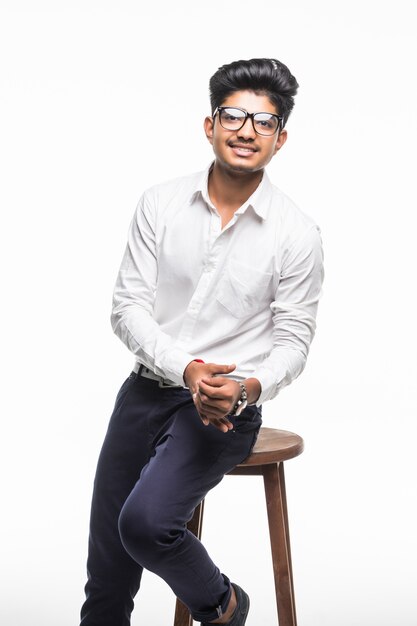 Handsome good looking Indian man sitting on a chair and relaxing, isolated for white wall