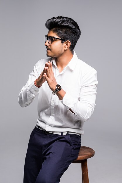 Handsome good looking Indian man sitting on a chair and relaxing, isolated for white wall