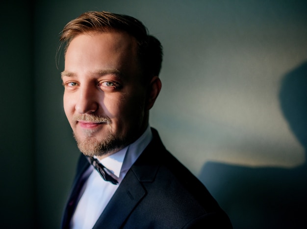 Free photo handsome groom in classy black suit stands in a dark room