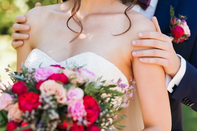 Handsome groom in dark blue suit gently holding beautiful bride with bridal bouquet