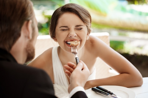 Sposo bello che alimenta la sua sposa di croissant in caffè.