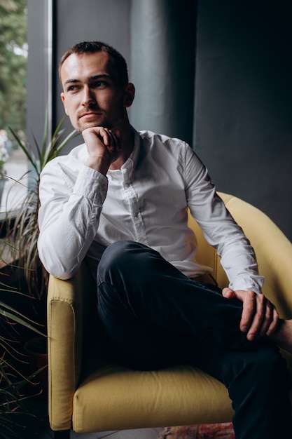 Free photo handsome groom looks thoughtful sitting on a couch in a cosy dark cafe