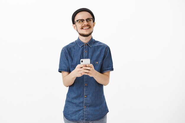 handsome guy being nostalgic remembering awesome moment from summer holidays while scrolling vacation photos looking at upper right corner dreamy and delighted with happy smile