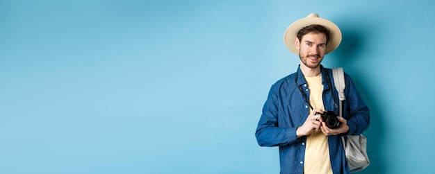 Free photo handsome guy going on summer vacation backpacking on holiday tourist with straw hat and camera smili