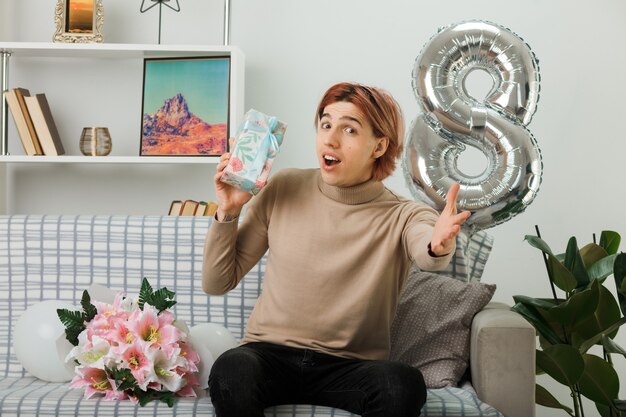 Free photo handsome guy on happy women day holding present sitting on sofa in living room