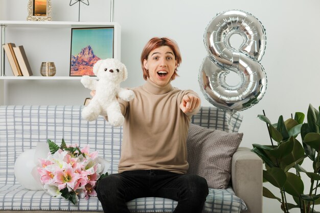Handsome guy on happy women day holding teddy bear sitting on sofa in living room