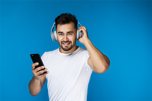 Handsome guy is listening music by headphones and holding cellphone in his arm