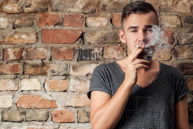 Красивый парень курит возле стены